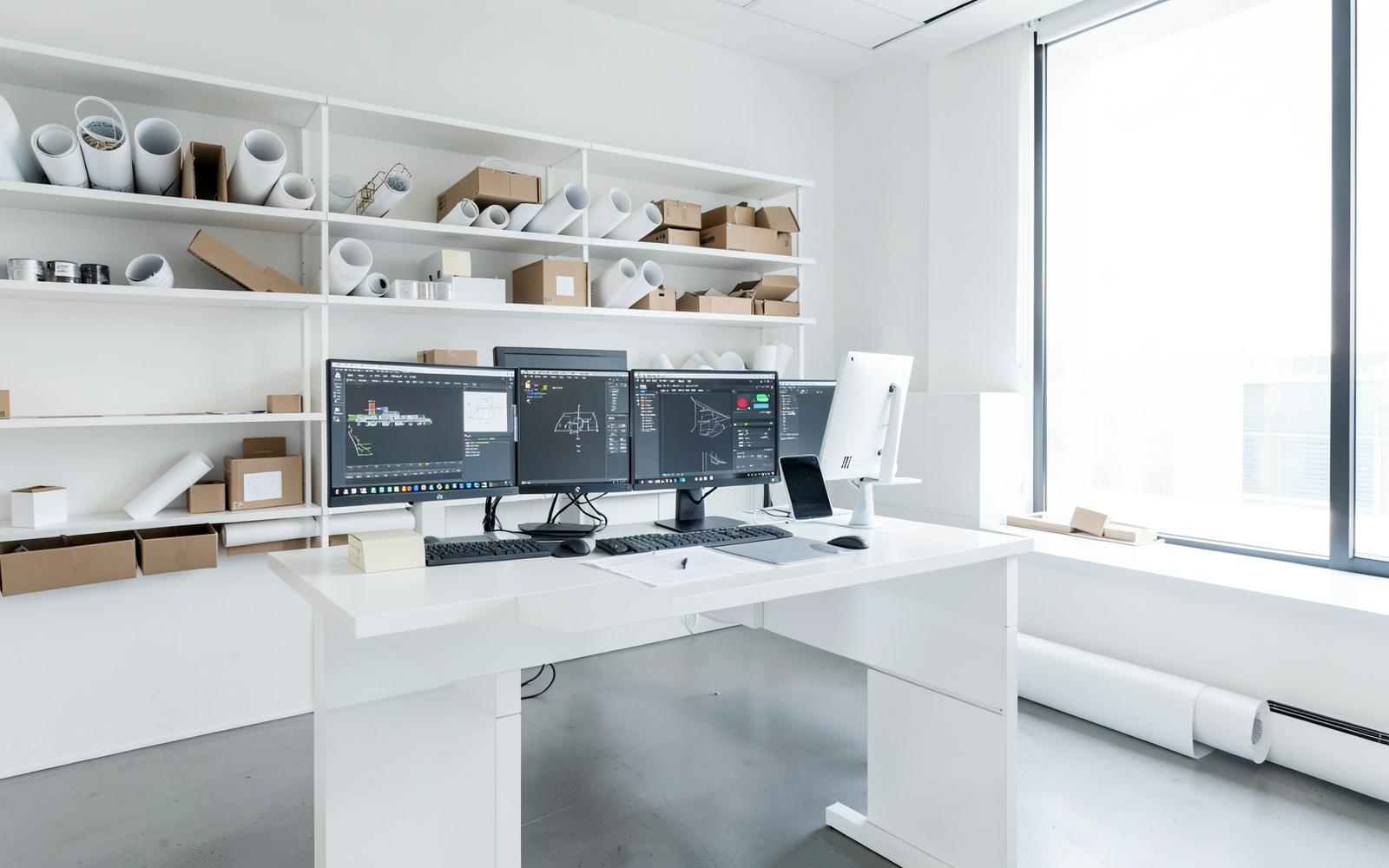 Heller Arbeitsplatz im Architekturbüro mit Planrollen und CAD-Bildschirmen